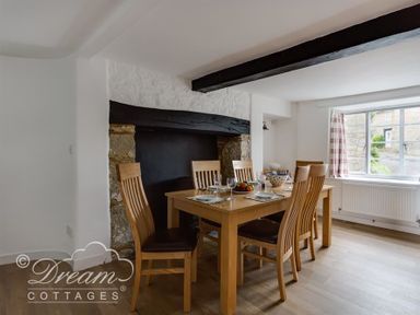 A dining room with a wooden table and six chairs near a window at Bramble Cottage in Burton Bradstock