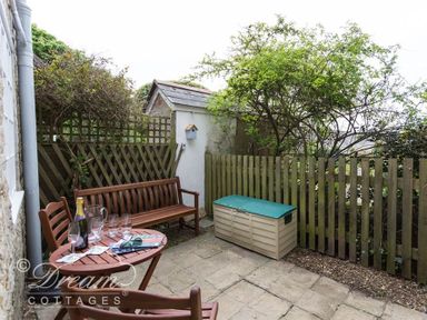 An outdoor patio with wooden bench and table with chairs near a wooden fence at Bramble Cottage in Burton Bradstock
