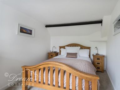 A bedroom with a wooden bed and two bedside tables with lamps at Bramble Cottage Burton Bradstock