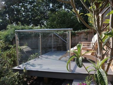 A wooden deck with two lounge chairs and glass railing surrounded by plants at Bramble Cottage in Burton Bradstock