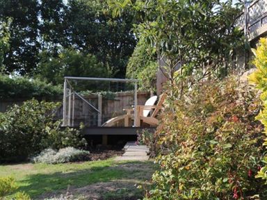 A garden with plants and a small deck with wooden chairs at Bramble Cottage in Burton Bradstock