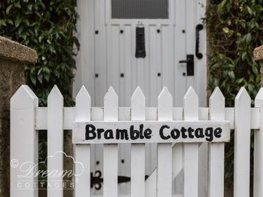 A white picket fence with a sign saying Bramble Cottage and a white door in the background at Bramble Cottage in Burton Bradstock