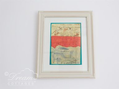 A framed child drawing with writing hanging on a white wall at Bramble Cottage in Burton Bradstock