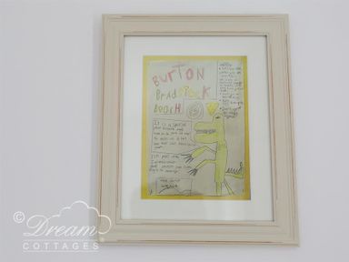 A framed drawing of a green dinosaur with text about Burton Bradstock beach on a white wall at Bramble Cottage Burton Bradstock