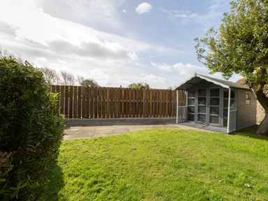 A garden with a wooden shed a tree a hedge and a wooden fence at Bramble Cottage in Burton Bradstock