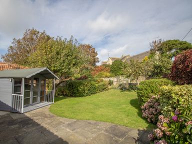 A garden with a small shed lawn trees bushes and flowers at Bramble Cottage in Burton Bradstock