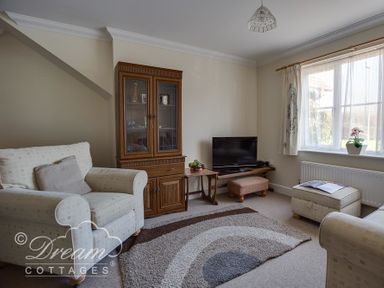 A living room with armchairs a wooden cabinet a television and a window at Bridge Apartment in Weymouth