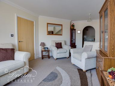 A living room with three armchairs a wooden cabinet and a small side table at Bridge Apartment in Weymouth