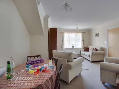 A sitting room with beige sofas a wooden cabinet and a dining table with art supplies at Bridge Apartment in Weymouth