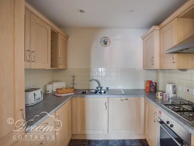 A kitchen with wooden cabinets a stainless steel sink toaster kettle and oven at Bridge Apartment in Weymouth