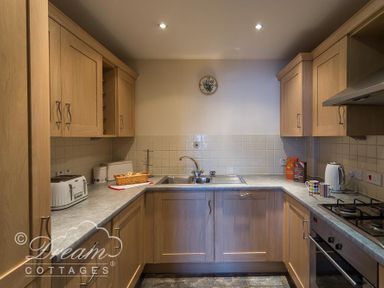 A kitchen with wooden cabinets a sink a toaster a kettle and a gas stove at Bridge Apartment in Weymouth