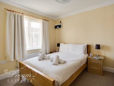 A bedroom with a double bed white linens rolled towels bedside tables lamps and a window with curtains at Bridge Apartment in Weymouth