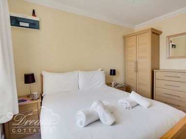 A bedroom with a double bed with white linens and rolled towels a wooden wardrobe and dresser Bridge Apartment Weymouth