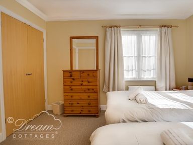 A bedroom with two beds a wooden chest of drawers with a mirror and a window with curtains at Bridge Apartment in Weymouth