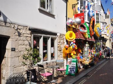 A shop with colorful beach toys and inflatables outside on a narrow street with tables and chairs at Bridge Apartment in Weymouth