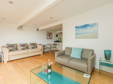 A living room with two sofas a glass coffee table with champagne and glasses a small dining table and chairs at Burton Bay in Burton Bradstock