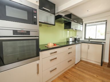 A kitchen with black and beige cabinets a bread loaf and tomato on the counter and a window at Burton Bay in Burton Bradstock