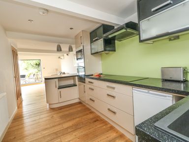 A kitchen with black countertops beige cabinets and green backsplash leading to a living area with wooden floor at Burton Bay in Burton Bradstock