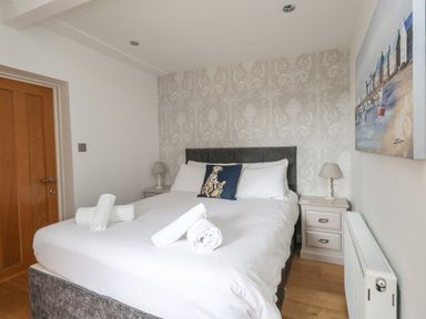 A bedroom with a double bed with white linens and rolled towels on a hardwood floor with a door and bedside tables Burton Bay Burton Bradstock