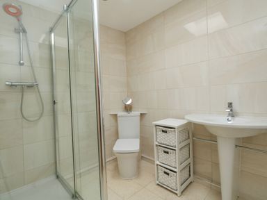 A bathroom with a glass shower enclosure toilet sink and a white storage unit with baskets at Burton Bay in Burton Bradstock