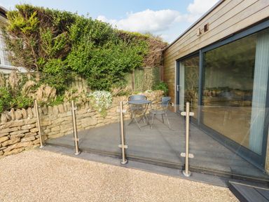 An outdoor patio area with a glass railing metal table and chairs stone wall and sliding glass doors at Burton Bay in Burton Bradstock