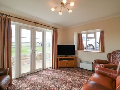 A living room with leather chairs a television on a wooden stand patterned carpet and French doors at Cliff Farm No 2 Cottage Burton Bradstock