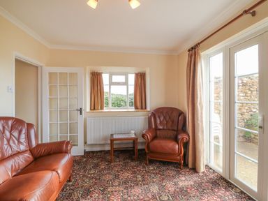A sitting room with leather chairs a small wooden table a window and glass doors at Cliff Farm No 2 Cottage Burton Bradstock
