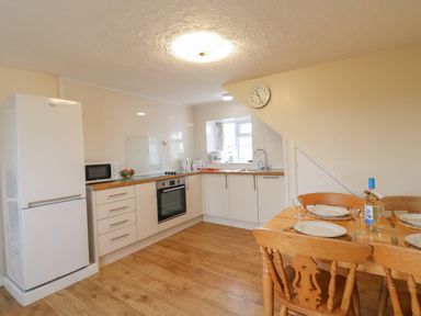 A kitchen with white cabinets a refrigerator oven microwave and a wooden dining table set with plates and glasses at Cliff Farm No 2 Cottage Burton Bradstock