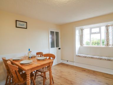 A dining room with a wooden table set with plates and wine glasses and a window seat at Cliff Farm No 2 Cottage Burton Bradstock