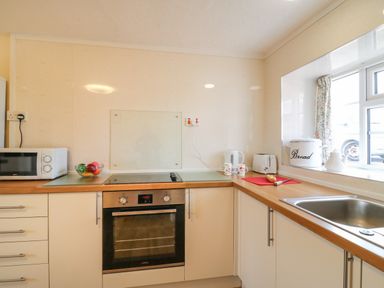 A kitchen with an oven, microwave, sink, kettle, toaster, bread bin, cutting board with knife and vegetables on the counter at Cliff Farm No 2 Cottage Burton Bradstock