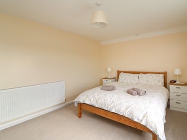 A bedroom with a wooden bed with floral bedding two bedside tables with lamps and a radiator at Cliff Farm No 2 Cottage Burton Bradstock