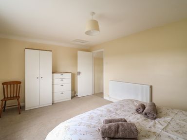 A bedroom with a bed folded towels white wardrobe chest of drawers wooden chair and an open door at Cliff Farm No 2 Cottage Burton Bradstock