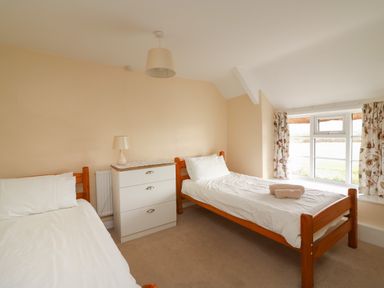 A bedroom with two single beds a white chest of drawers and a window with floral curtains at Cliff Farm No 2 Cottage Burton Bradstock