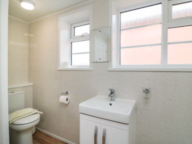 A bathroom with a toilet a sink with cabinet two windows and a mirror at Cliff Farm No 2 Cottage Burton Bradstock