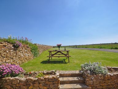 A picnic table with flowers and wine on a lawn with stone walls and flower beds at Cliff Farm No 2 Cottage Burton Bradstock