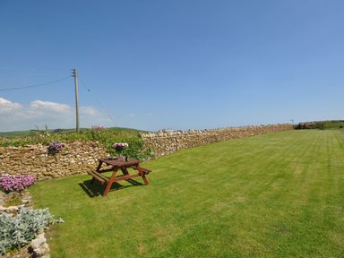 A garden with a wooden picnic table on a lawn and a stone wall with flowers at Cliff Farm No 2 Cottage in Burton Bradstock