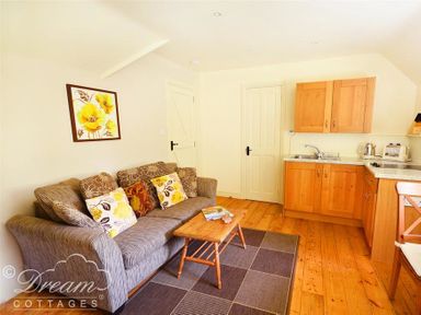 A living room with a sofa having floral cushions a wooden coffee table and a kitchen area with wooden cabinets at Coombe Orchard in Swanage