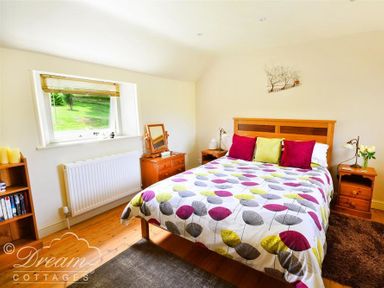 A bedroom with a double bed colorful bedspread and wooden furniture at Coombe Orchard in Swanage