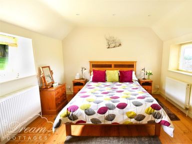 A bedroom with a double bed with patterned duvet and cushions beside wooden bedside tables at Coombe Orchard in Swanage
