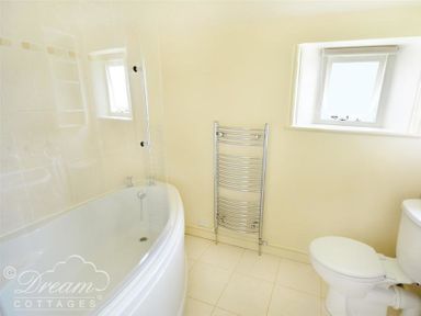 A bathroom with a corner bathtub a toilet a heated towel rail and two small windows at Coombe Orchard in Swanage