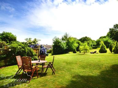A garden with a wooden table and chairs on a lawn surrounded by bushes and trees at Coombe Orchard Swanage