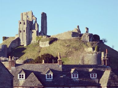 Ruins of a castle on a grassy hill behind rooftops with chimneys at Coombe Orchard in Swanage