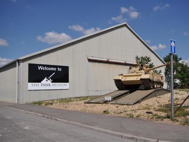 An outdoor display of a tank on ramps next to a building with a sign that says Welcome to The Tank Museum