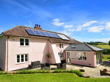 A two story house with solar panels on the roof and outdoor seating on a patio at Culverwells in Axminster