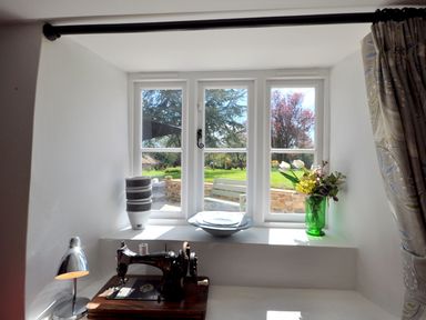 A window with a stack of bowls a sewing machine a plate and a vase with flowers at Culverwells in Axminster