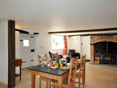A dining area with a wooden table set for breakfast four chairs and a brick fireplace with a wood stove at Culverwells in Axminster