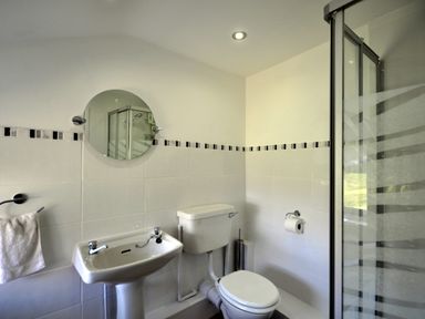 A bathroom with a sink towel holder toilet paper holder toilet shower with glass door and round mirror at Culverwells in Axminster