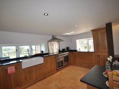 A kitchen with wooden cabinets a double oven a white sink and windows showing a garden at Culverwells in Axminster