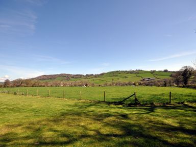 A grassy field with a wire fence and hills in the background at Culverwells in Axminster