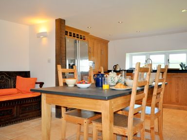 A kitchen with a wooden dining table set with teapot croissant and orange juice wooden chairs and an orange cushioned bench at Culverwells Axminster